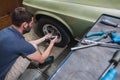 Young man removing wheels or tires from an old vintage car from the 60s or 70s in his home garage. Tools are seen around Royalty Free Stock Photo