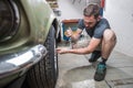 Young man removing wheels or tires from an old vintage car from the 60s or 70s in his home garage. Tools are seen around Royalty Free Stock Photo