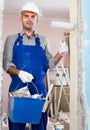 young man repairer working with roller in uniform, gloves and helmet