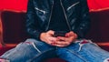 Young man resting with smartphone on small red sofa. Close-up of male body part sitting on armchair with mobile phone in