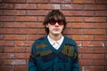 Young man with retro round sunglasses standing before brick wall, exuding vintage aura Royalty Free Stock Photo