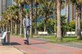 Young man riding electric scooter eco friendly transport along the promenade in the city with palm trees. Male driving e Royalty Free Stock Photo