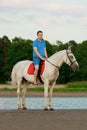 Young man riding a horse at sunset on the beach. Man with a horse in the rays of the sun by the sea. Royalty Free Stock Photo