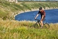 Young man riding mountain bike on the green meadow above the blue river in the countryside. Royalty Free Stock Photo