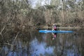 A young man rowing on a blue canoe on a calm river along the ban Royalty Free Stock Photo