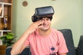 Young man rubbing eyes due to over use of VR or virtual reality goggles or headset at home while on sofa - concept of