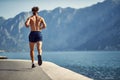 Young man running on jetty by water. Outdoors workout. Sport, vitality, recreation concept