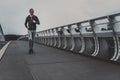 Young man running on the modern bridge in the city, listening music on smartphone