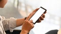 Young man`s hands while using/holding a cropped black smartphone with white blank screen.