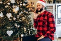 Young man in Santa Claus hat talking on cell phone at home against background of Christmas tree Royalty Free Stock Photo