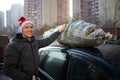 A man in Santa Claus hat tying a Christmas tree to the roof of the car to bring it home Royalty Free Stock Photo