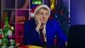 Young man in santa hat works on laptop, sitting in office. Sad businessman in modern workplace in New Year's atmosphere. Royalty Free Stock Photo