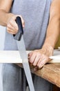 Young man sawing a wooden board with a handsaw