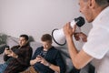 Young man screams through a megaphone at friends which using a mobile phone