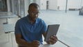 Young man with serious expression looking at tablet in modern office setting, surrounded by natural light and minimalist decor, Royalty Free Stock Photo