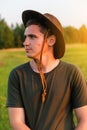 Young man serious farmer in cowboy hat at agricultural field on sunset with sun flare. Profile portrait of man standing