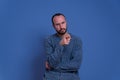 Young man with severe and angry expression pointing finger in sign of accuse with beard and casual clothing. in studio with blue