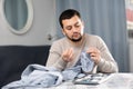 Young man sewing on buttons on sleeve of shirt at home table