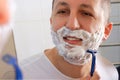 A young man shaves with a razor in front of a mirror. Royalty Free Stock Photo