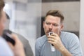 Young man shaves with razor in front of mirror Royalty Free Stock Photo