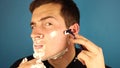 A young man shaves standing on a blue background