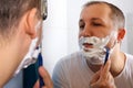 Young man shaving in front of a mirror in the bathroom. Skin care concept Royalty Free Stock Photo