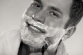 Young man shaving using razor with cream foam. Royalty Free Stock Photo