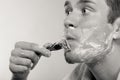 Young man shaving using razor with cream foam. Royalty Free Stock Photo