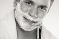 Young man shaving using razor with cream foam. Royalty Free Stock Photo