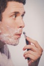 Young man shaving using razor with cream foam. Royalty Free Stock Photo