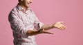 Young man in shirt have a dialog gesticulating with open hands palms smiling on pink