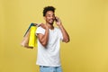 Young man with shopping bags talking on smart phone isolated on yellow background Royalty Free Stock Photo