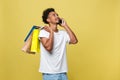 Young man with shopping bags talking on smart phone isolated on yellow background Royalty Free Stock Photo