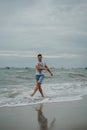 A young man in shorts and a t-shirt is having fun and actively playing with the sea. Running, jumping and having fun at Royalty Free Stock Photo