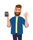 Young man showing or holding digital calculator device in hand and gesturing, making okay or OK sign while winking eye. Good. Royalty Free Stock Photo