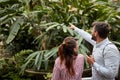 Young man showing with index finger different plants to a female, explaining, enjoying, smiling. Copy space