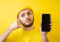 Young man, shows a call back sign on a mobile phone. Isolated on a yellow background