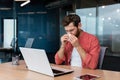 A young man is sick at work. sits in the office, wipes his nose with a napkin, has a runny nose