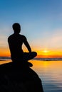 Man silhouette sitting on stone at the seaside contemplating sun Royalty Free Stock Photo