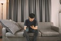 Young man sit down on the sofa while using mobile phone and drink coffee  relaxing at home Royalty Free Stock Photo