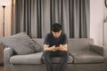 Young man sit down on the sofa while using mobile phone and drink coffee  relaxing at home Royalty Free Stock Photo