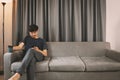 Young man sit down on the sofa while using mobile phone and drink coffee  relaxing at home Royalty Free Stock Photo