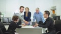 Young man sit at a table and show something on tablet to his workmates