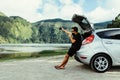 Young man sits in the car trunk take selfie photo on phone near beauty lake background. Summer vocation. Car trip Royalty Free Stock Photo