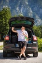 Young travel man sits in the car trunk take selfie photo on phone on mountaind background Royalty Free Stock Photo