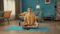 A young man sits cross legged in a lotus position with his eyes closed on a sports mat next to a smartphone. A man in a