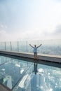 Young man with raised haands on a glass floor on the roof of a King Power Mahanakhon building