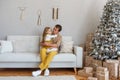 Young man sits on sofa with little girl near Christmas tree. Single parent celebrating Christmas