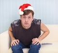 Young man sits on sofa in a red Christmas cap Royalty Free Stock Photo