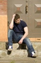 A young man sits on the stairs near the house